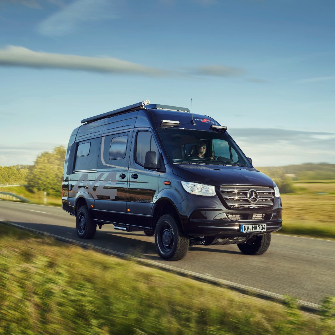 Malibu Genius 4x4 Offroad Campervan Ein moderner Kastenwagen fährt auf einer Landstraße in ländlicher Umgebung. Malibu Genius 4x4 Offroad Campervan